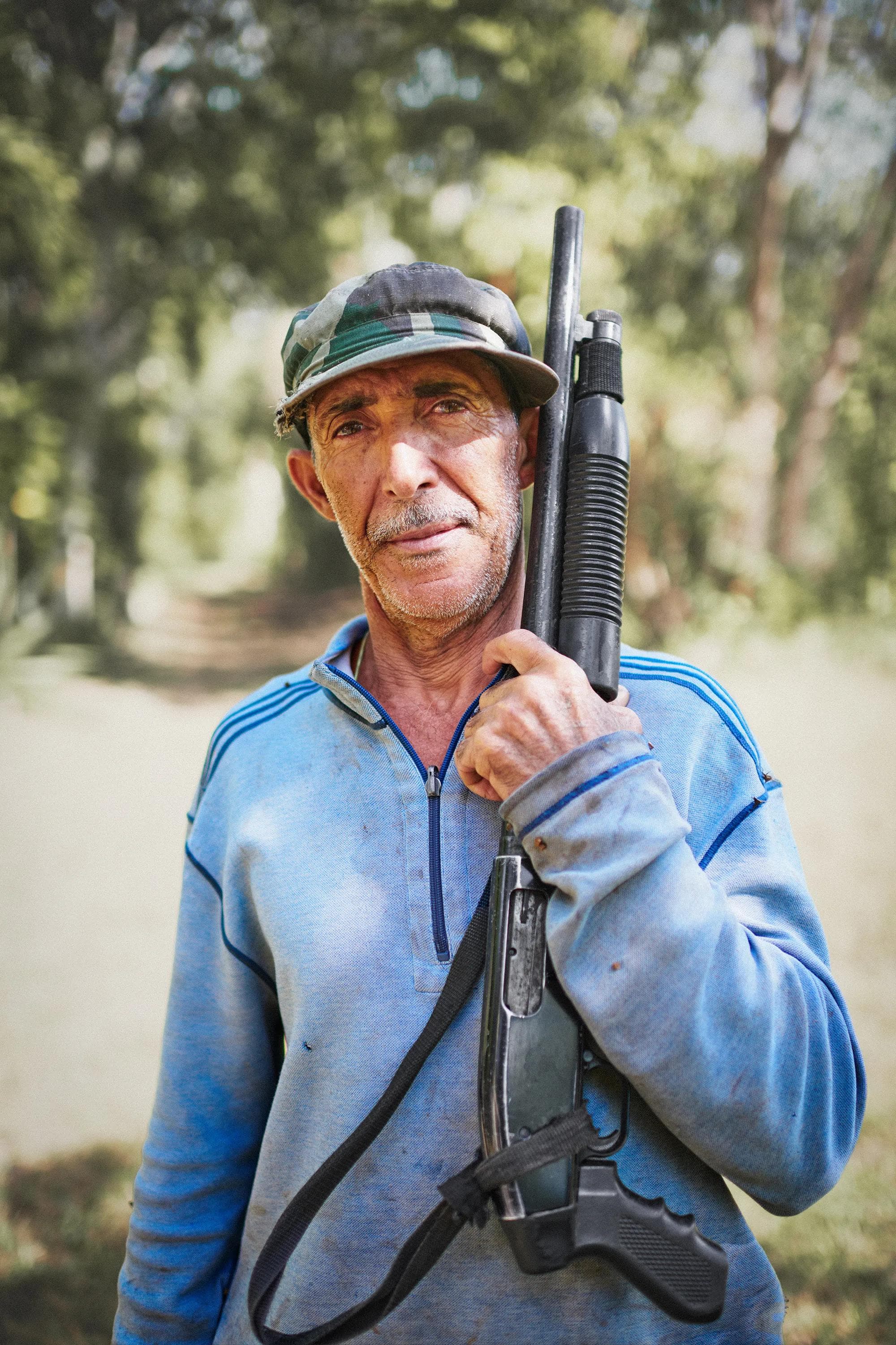 elderly farmer standing with machete and boots in tropical landscape, environmental portrait in Dominican Republic