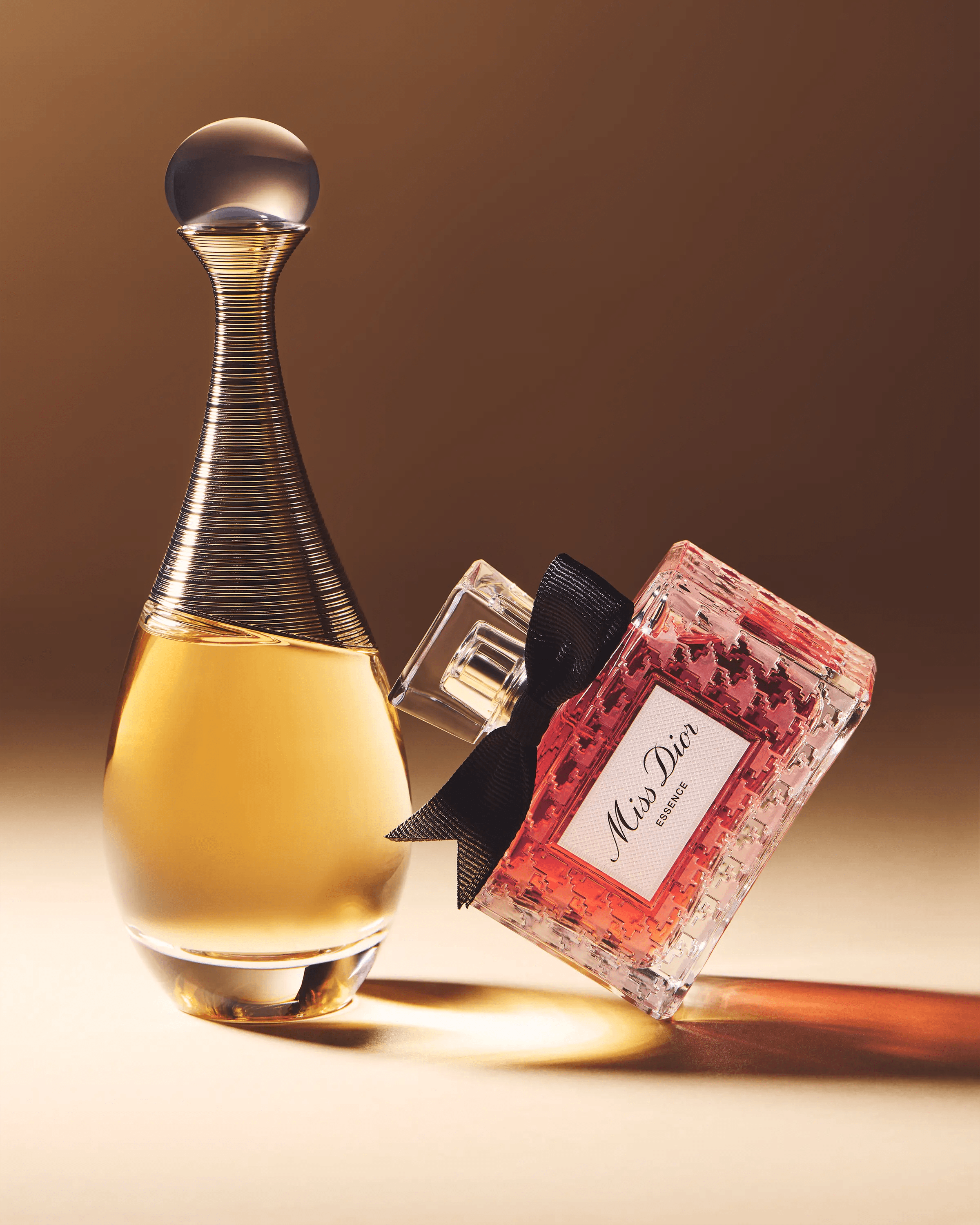 J'adore and Miss Dior Essence fragrance bottles styled together on warm gradient surface, editorial luxury fragrance photography London