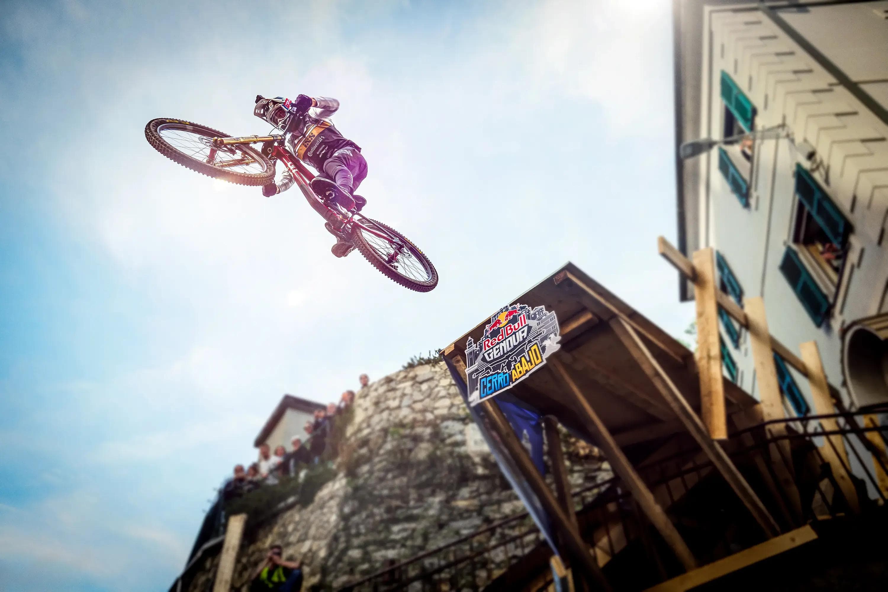 mountain biker performing jump over ramp with red bull branding, low angle perspective, sports event photography