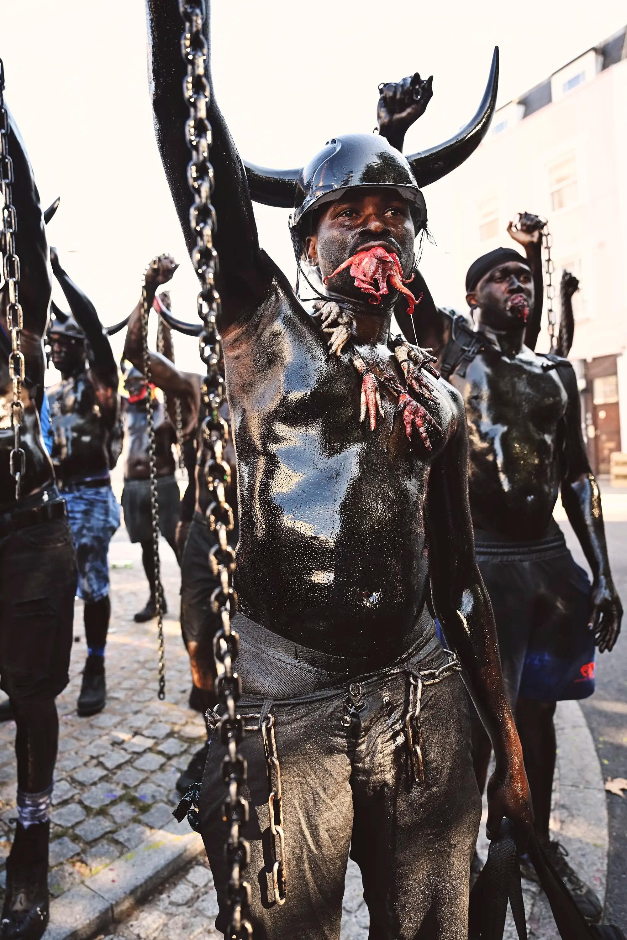 Jab Jab carnival performer holding chains while covered in black body paint during street procession