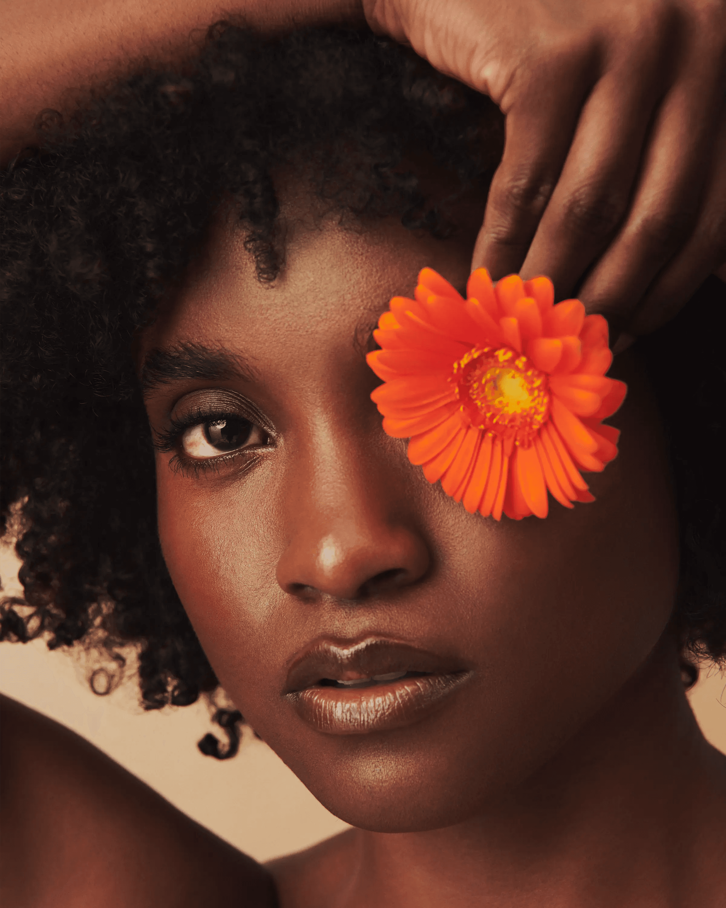 editorial portrait of female model with orange gerbera flower placed over one eye, considered composition, fashion campaign photography London