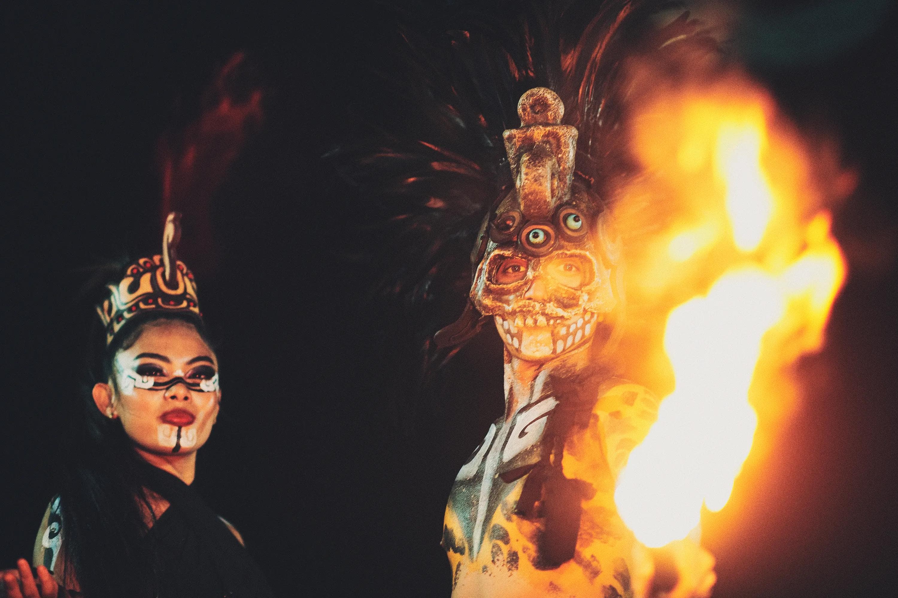 masked performer beside a large flame during a contemporary ritual spectacle inspired by Mayan imagery