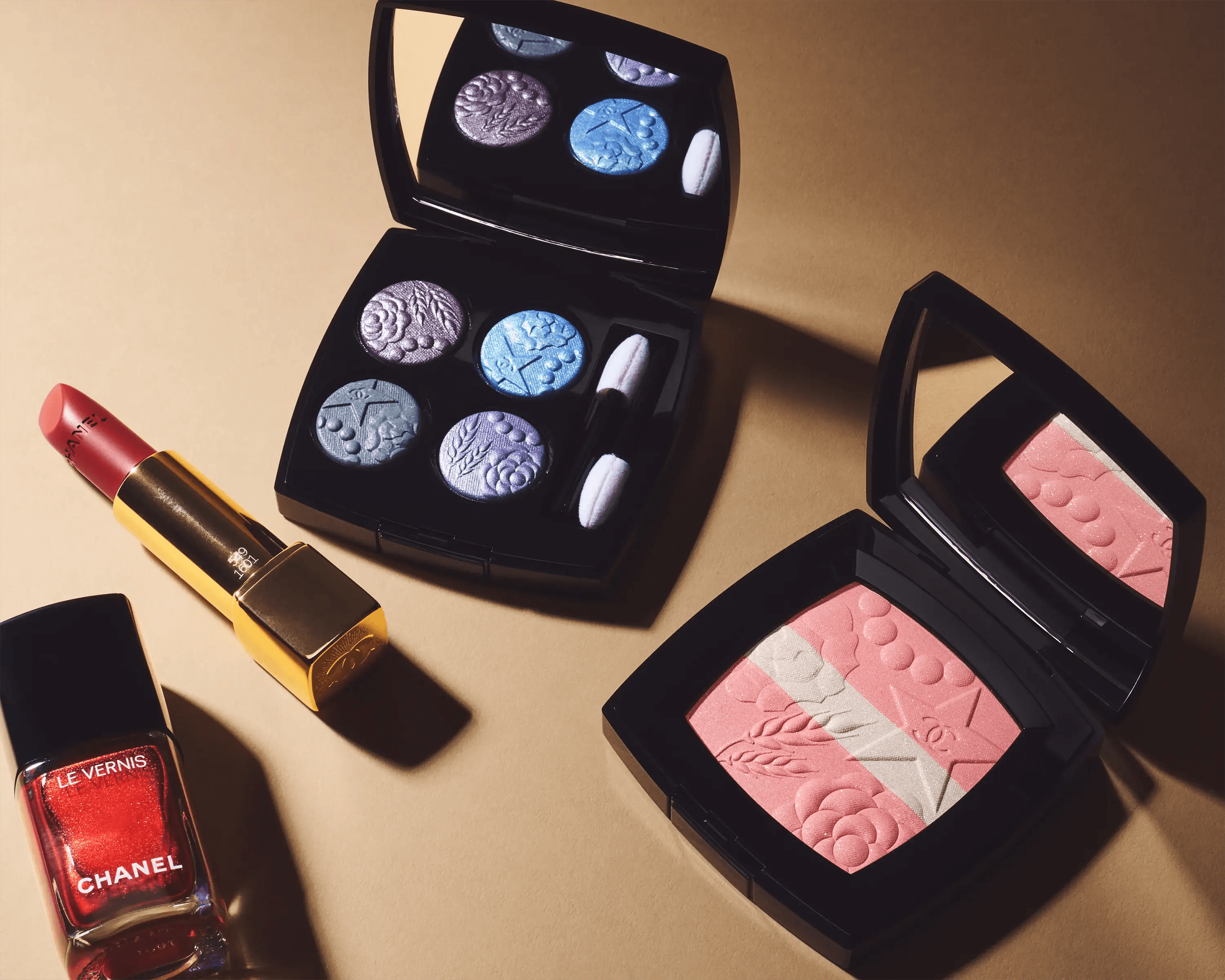 Chanel Les 4 Ombres eyeshadow palette, Rouge Coco lipstick and Le Vernis nail colour arranged on warm surface with directional shadow, luxury beauty still life photography London