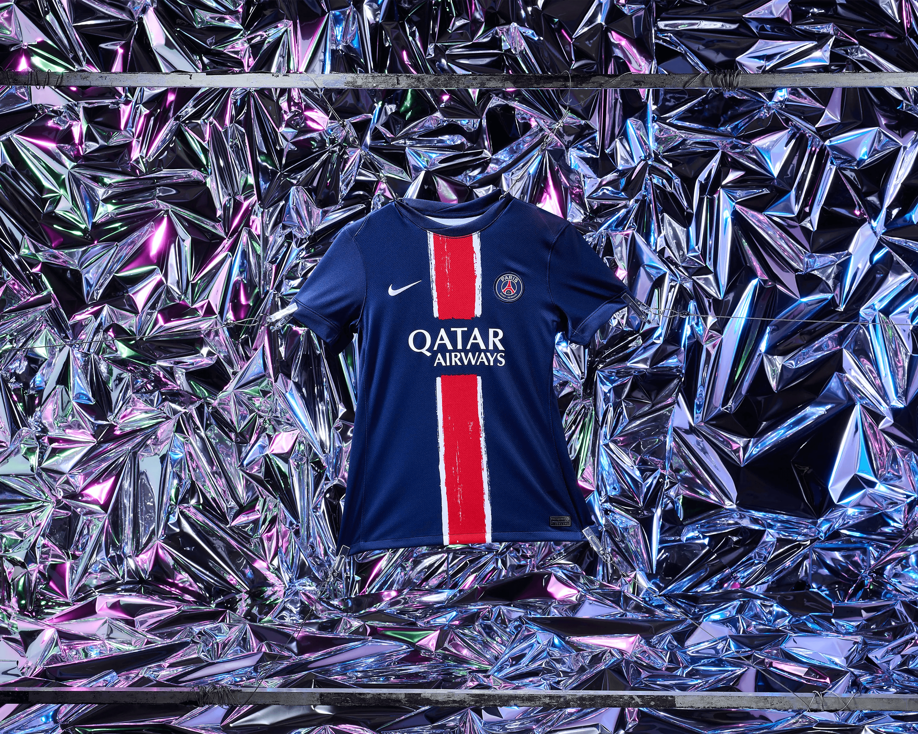 PSG home kit suspended on clips against full holographic silver and pink backdrop, commercial sportswear still life photography Manchester