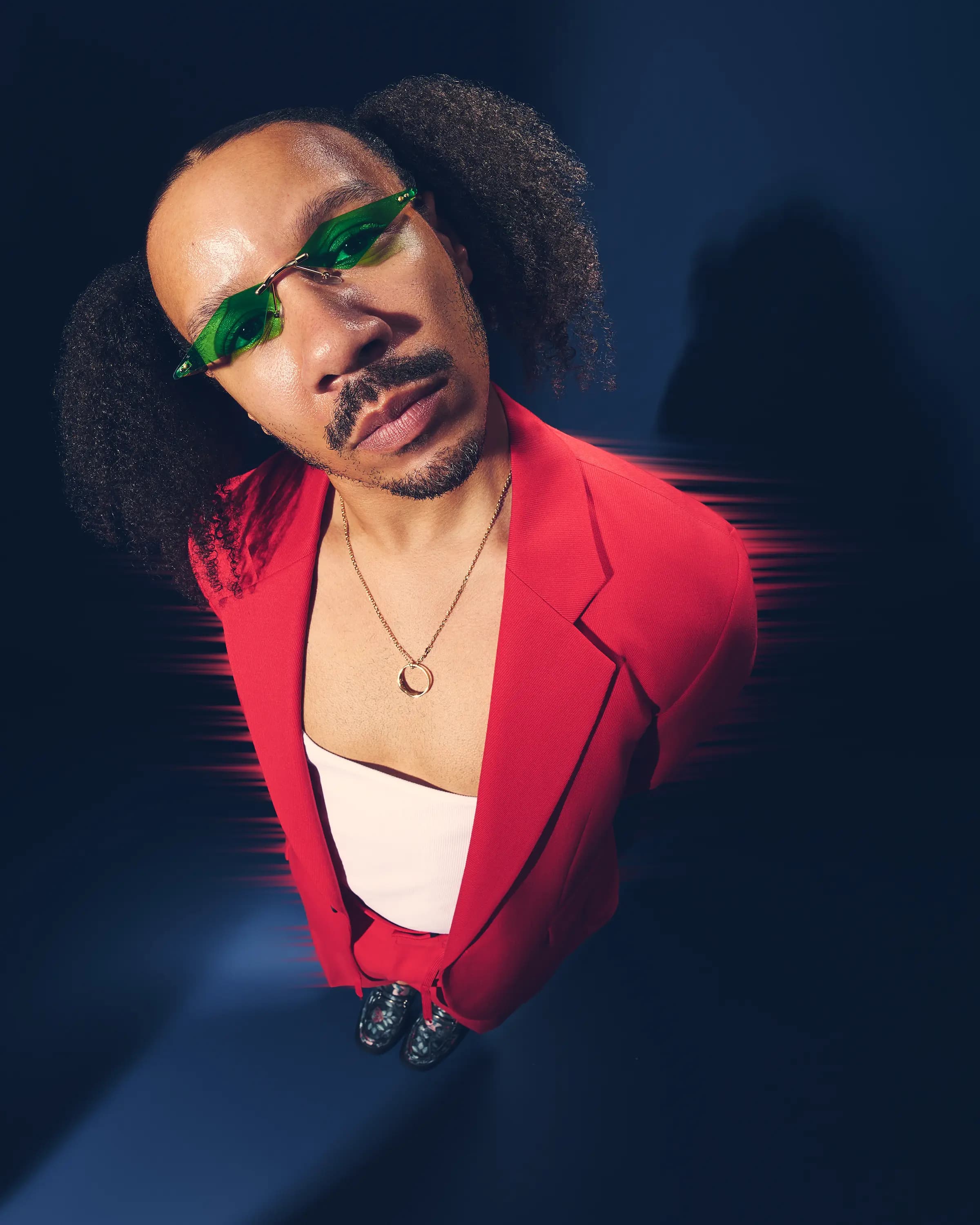 portrait en gros plan d'un mannequin homme en blazer rouge avec lunettes de soleil teintées vertes, flou de mouvement rouge, portrait de mode éditorial à Londres