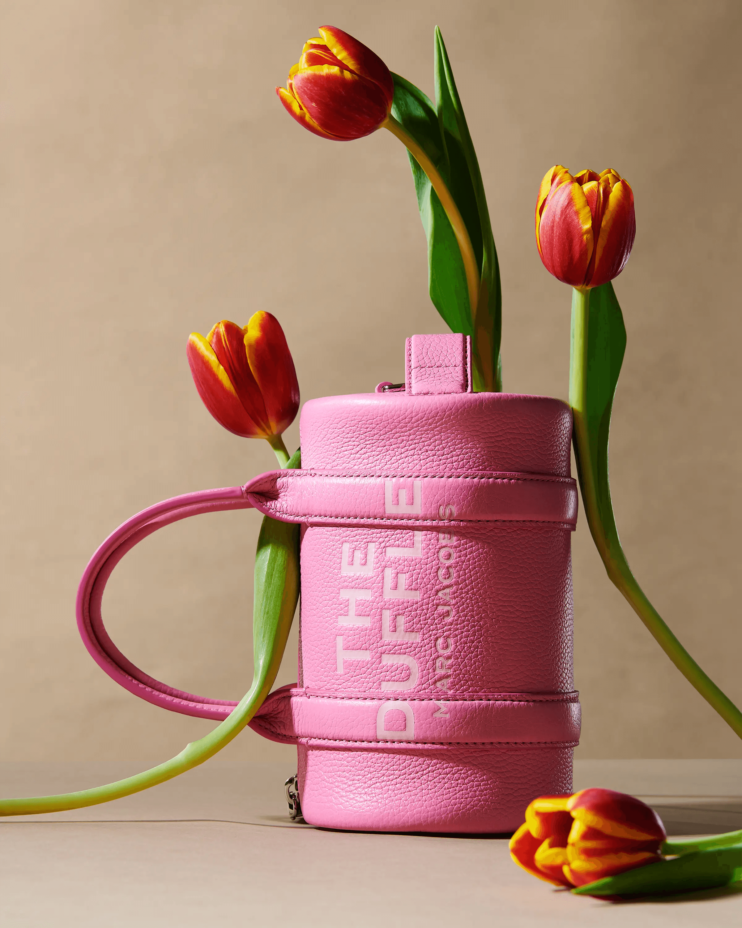 pink Marc Jacobs The Duffle bag with red and yellow tulips emerging from top, wide shot, luxury accessories still life photography London