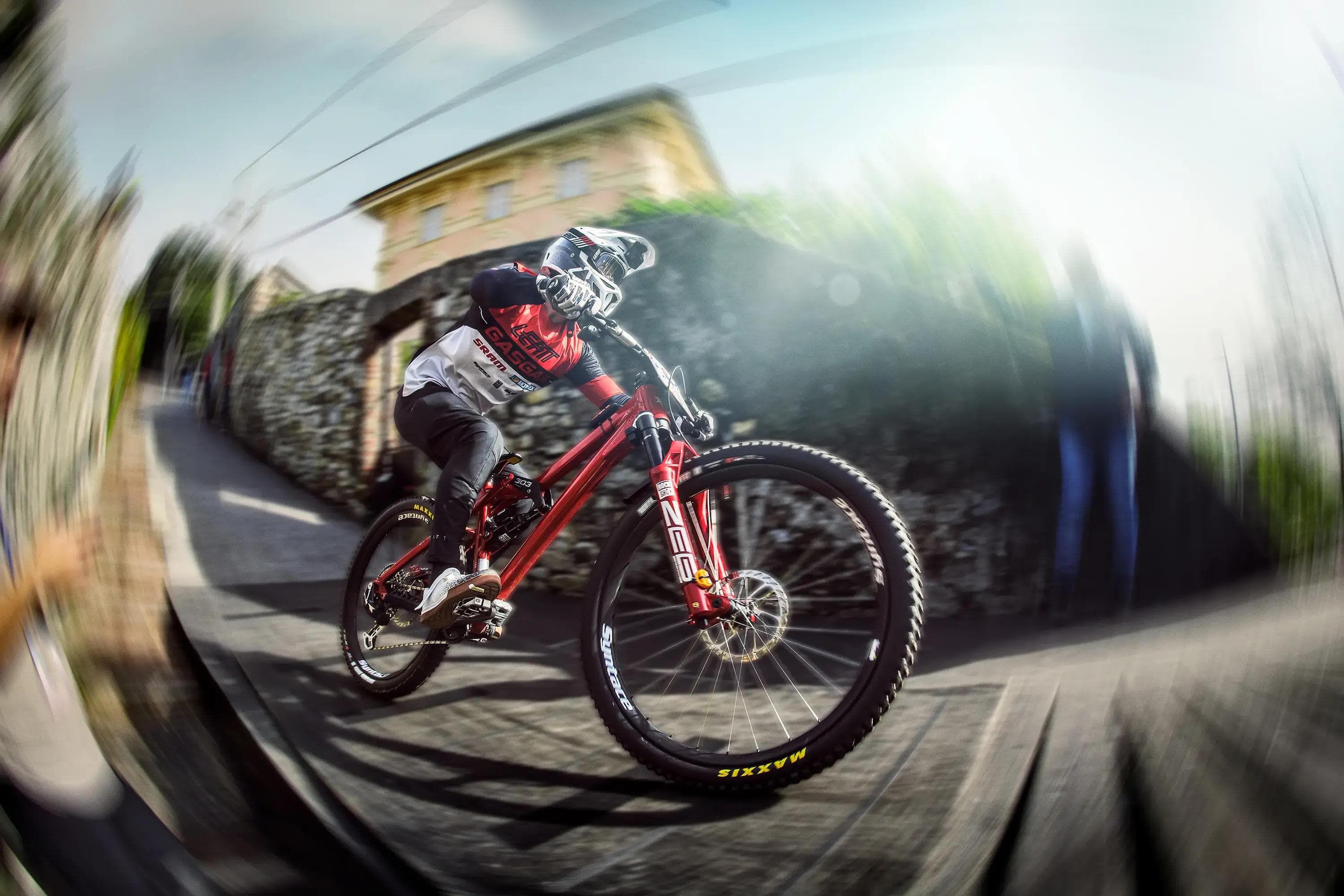 downhill rider racing through narrow street corner with motion blur, immersive angle, mtb photography