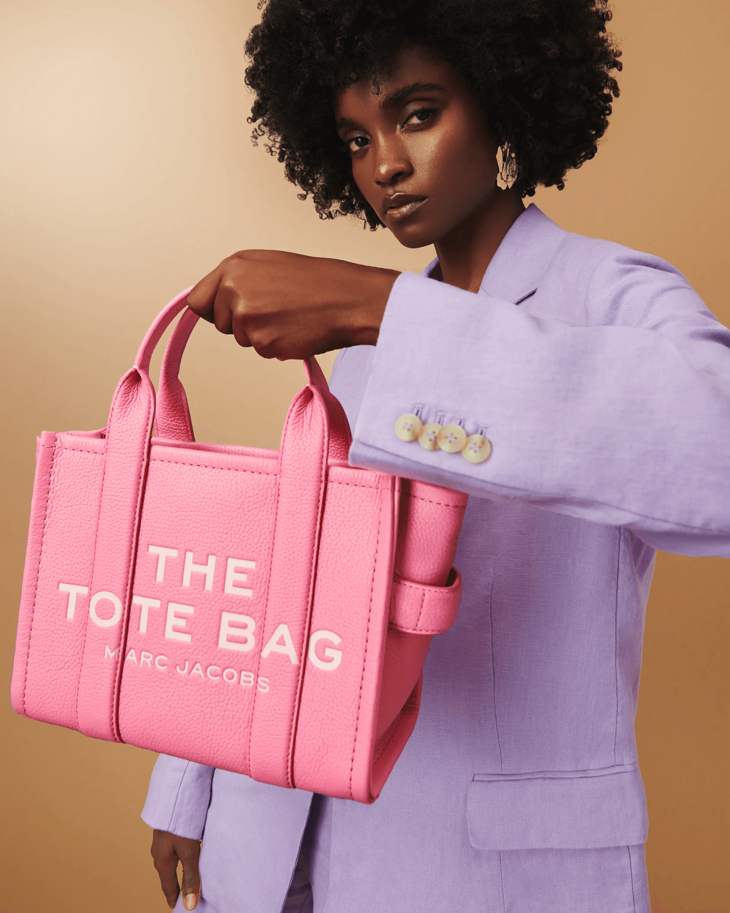 female model in lilac blazer presenting pink Marc Jacobs The Tote Bag, clean editorial composition, luxury fashion campaign photography London