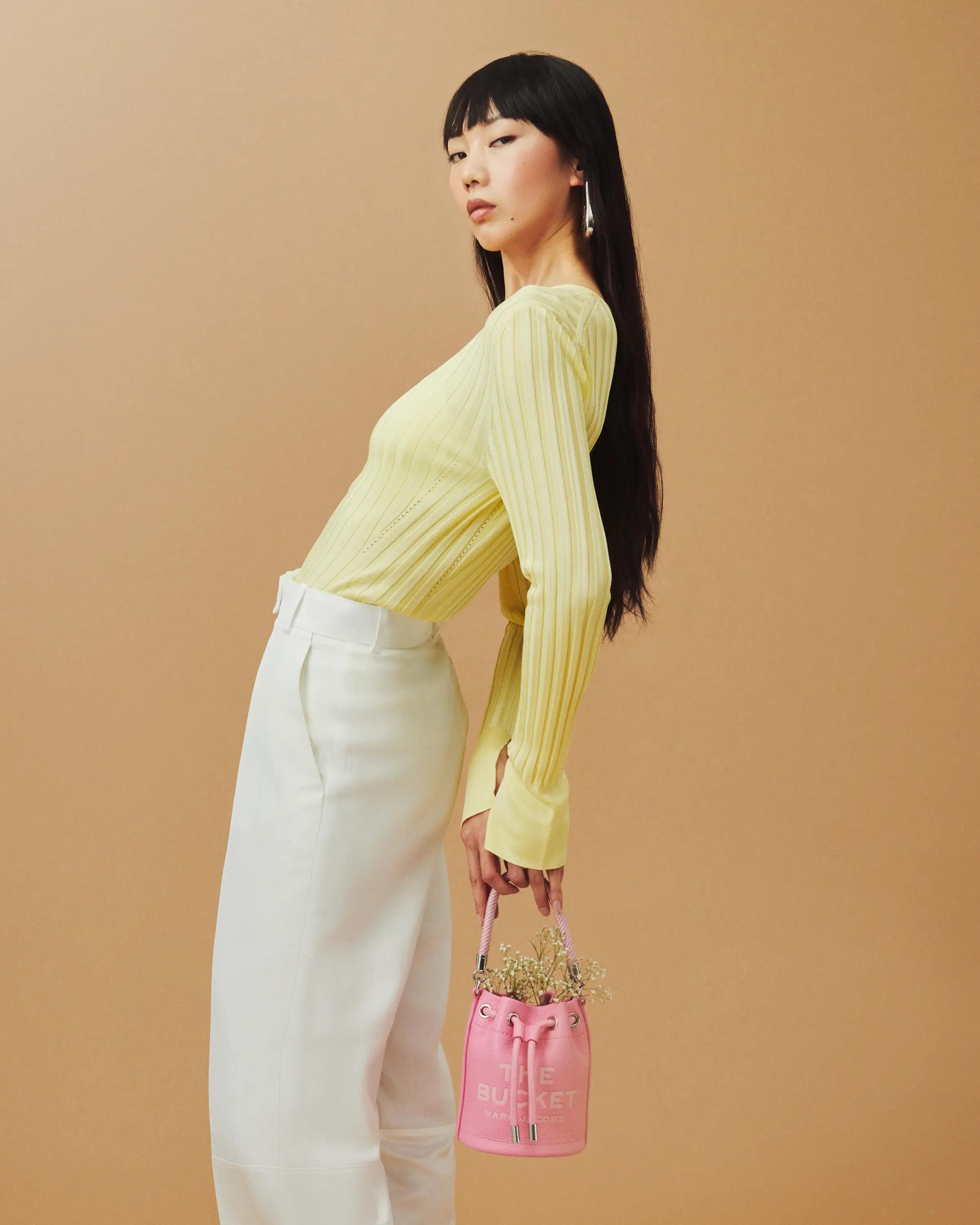 full length studio portrait of female model in yellow knit holding pink Marc Jacobs The Bucket bag, editorial fashion photography London