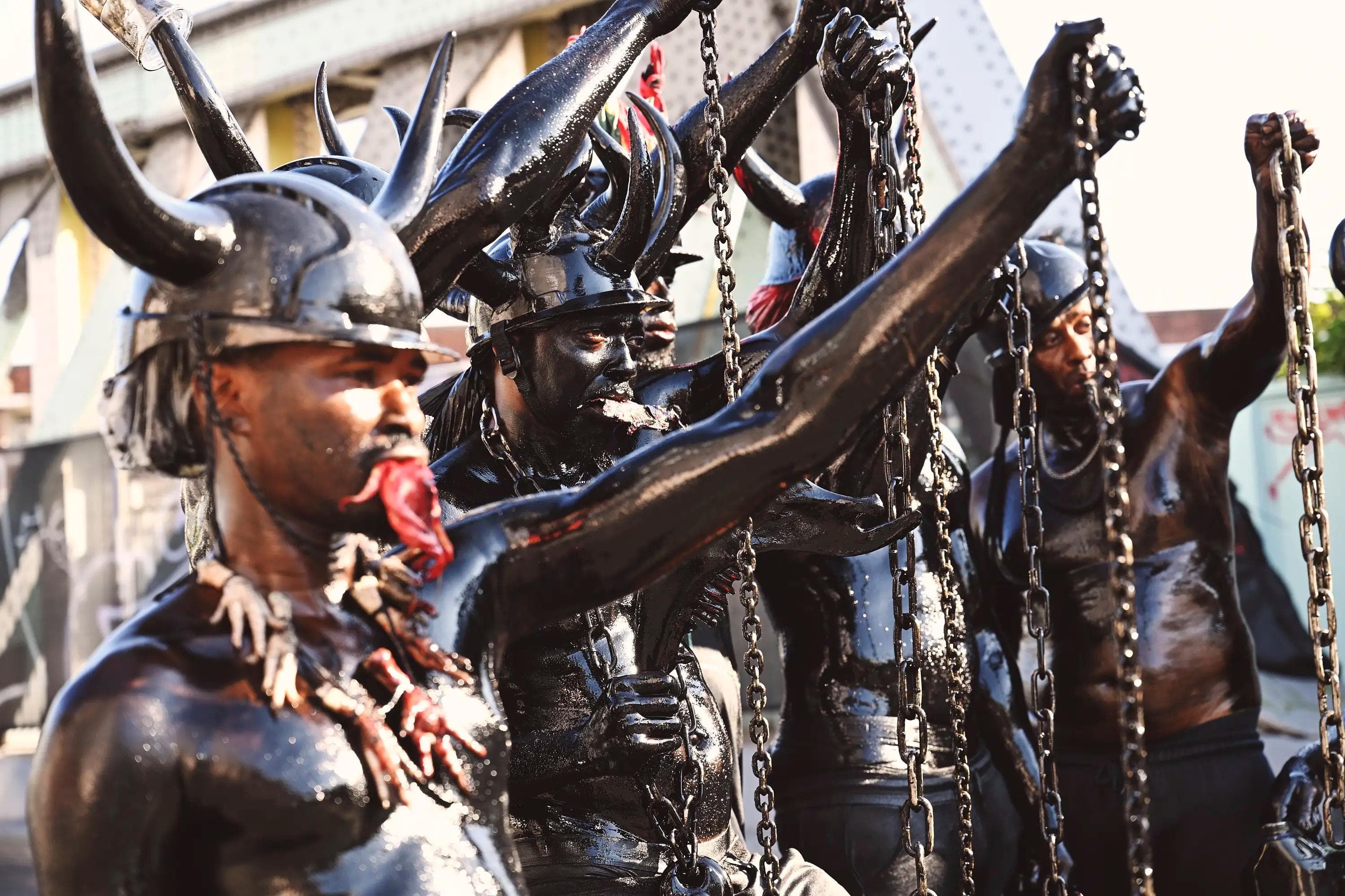 group of Jab Jab performers raising chains while covered in black oil and wearing horned helmets