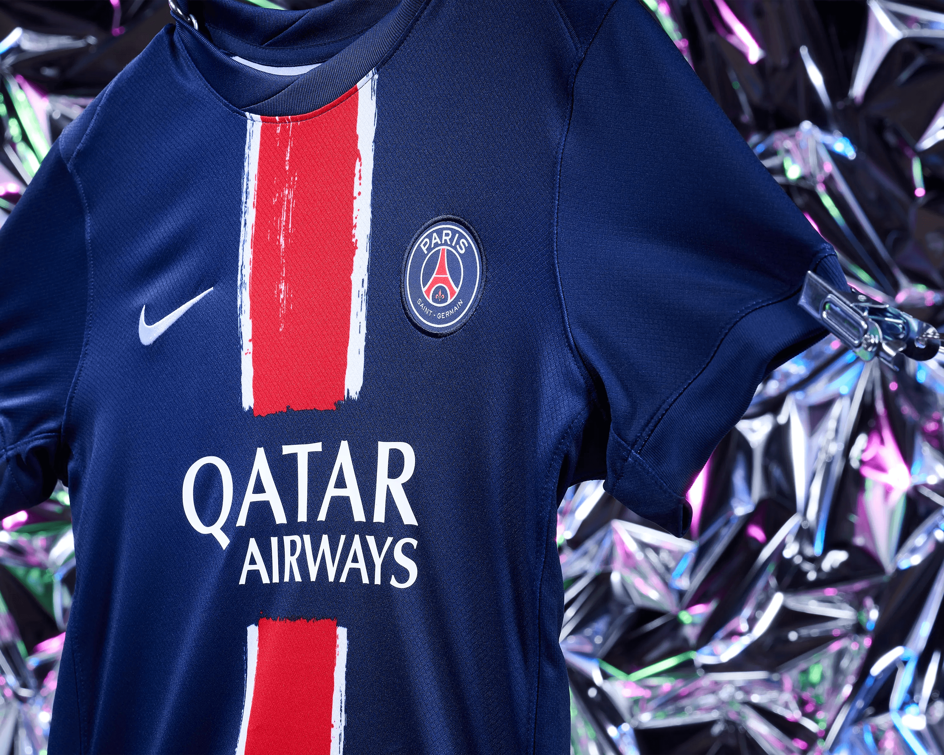 close up of PSG home kit badge and red stripe with holographic silver backdrop, commercial sportswear still life photography Manchester