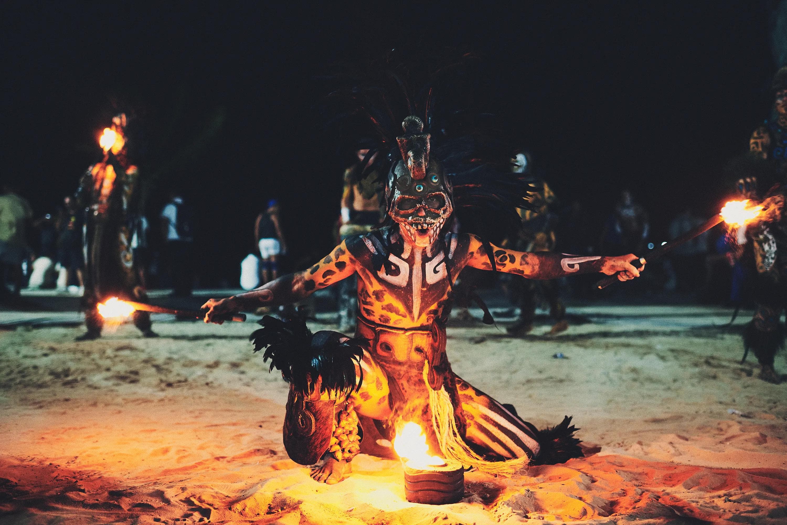 masked fire performer with skeletal face paint holding flaming torches during a staged ritual inspired by Mayan traditions