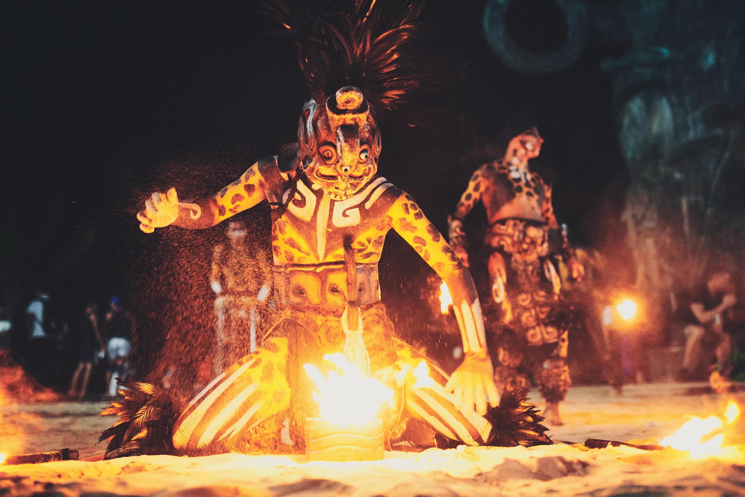 ceremonial performer illuminated by firelight kneeling in the sand during a night performance in Mexico