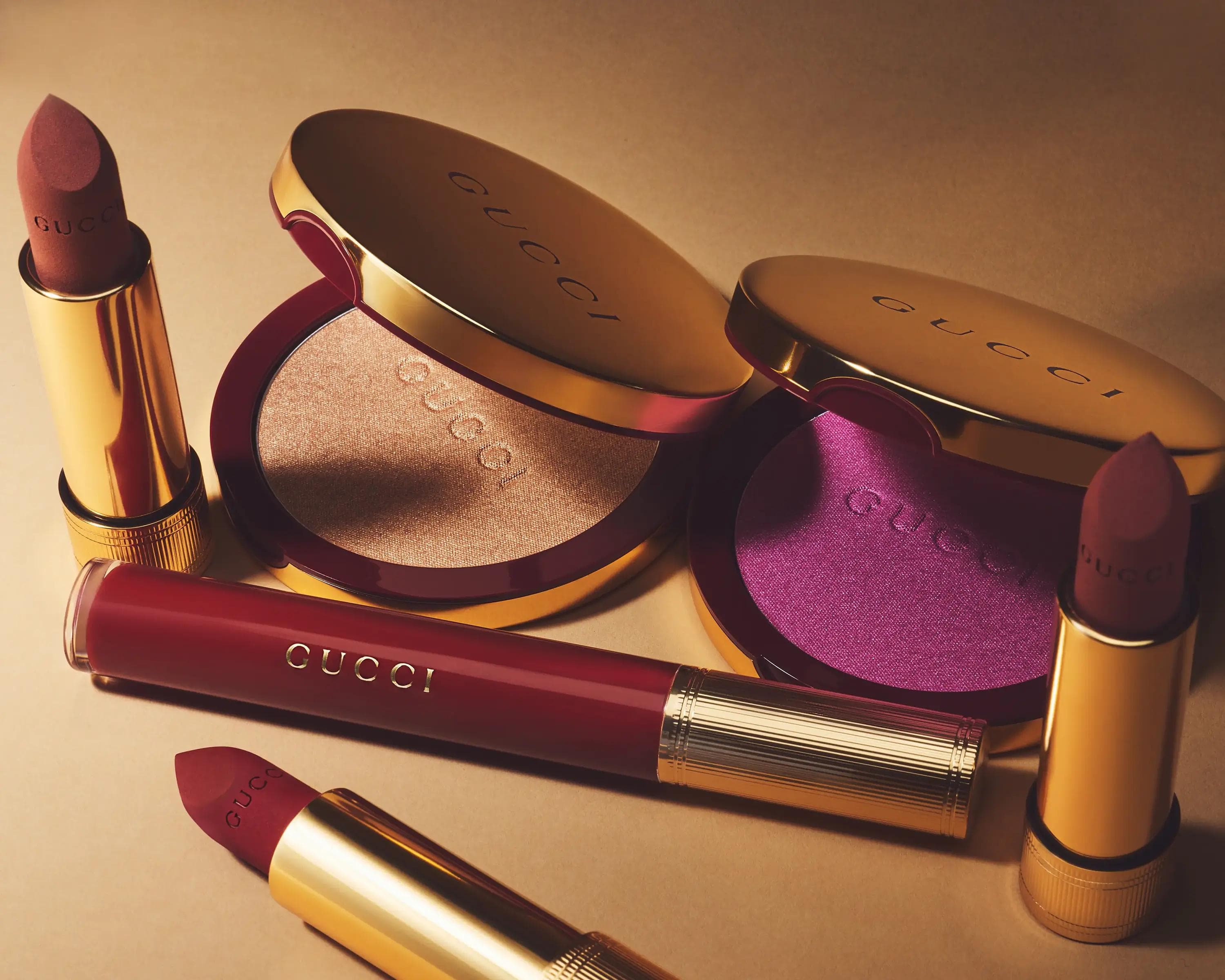 Gucci lipsticks and powder compacts in burgundy and gold arranged on warm surface, luxury beauty still life photography London