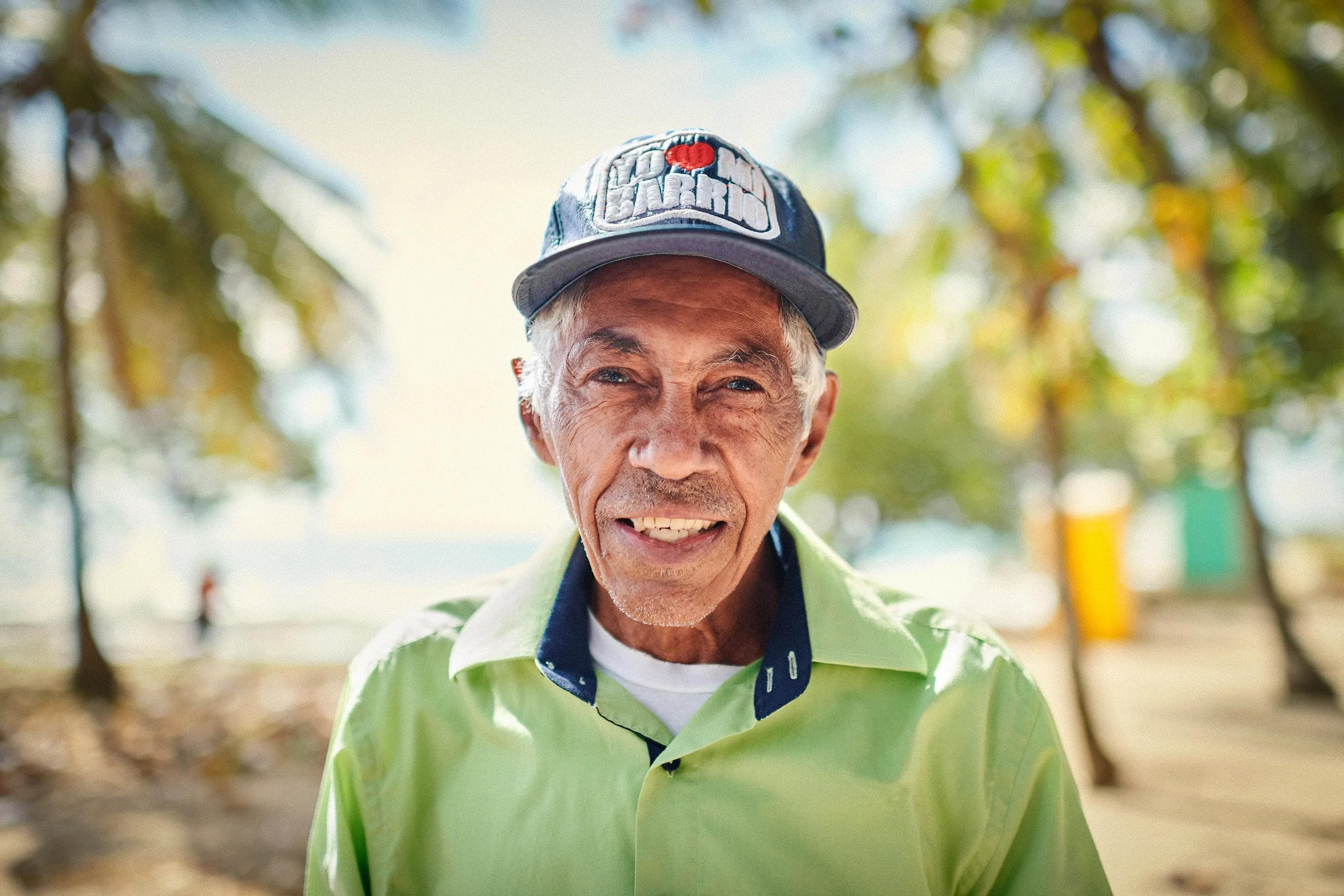 older man smiling outdoors in tropical sunlight wearing green shirt and cap, documentary portrait photography