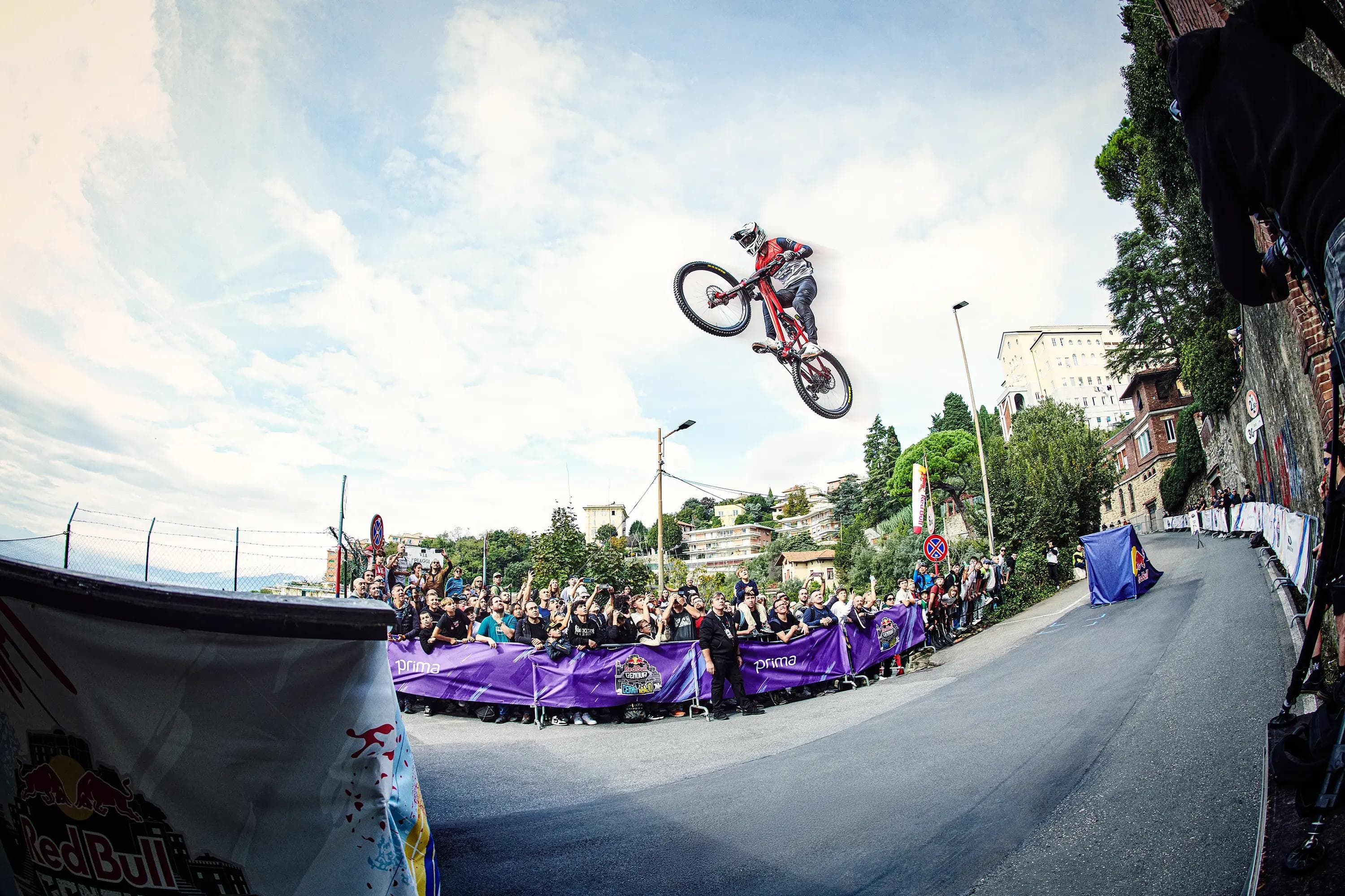 rider airborne above street with spectators behind barriers, wide scene, action sports photography