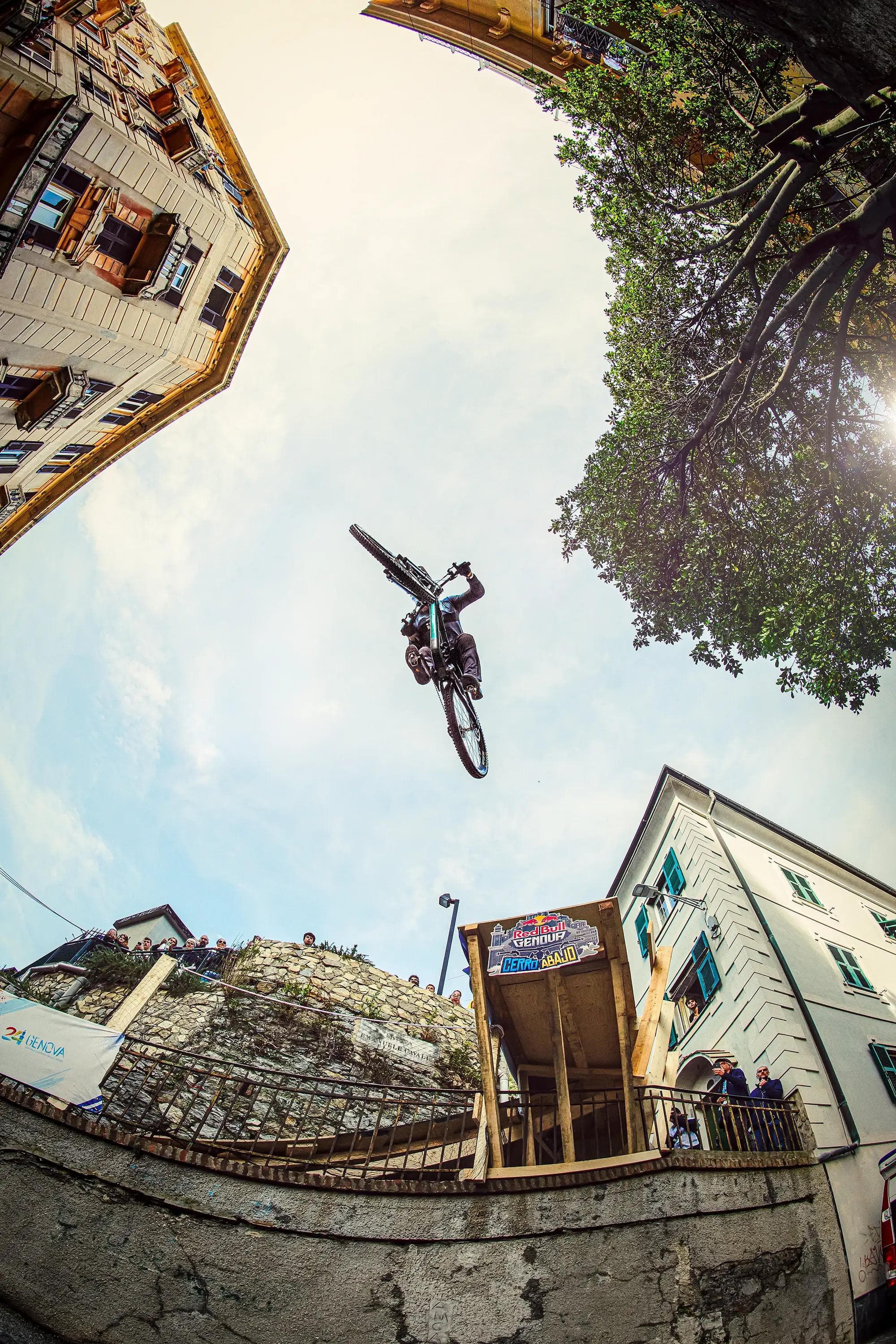 mountain biker captured from below between buildings mid jump, dramatic composition, extreme sports photography