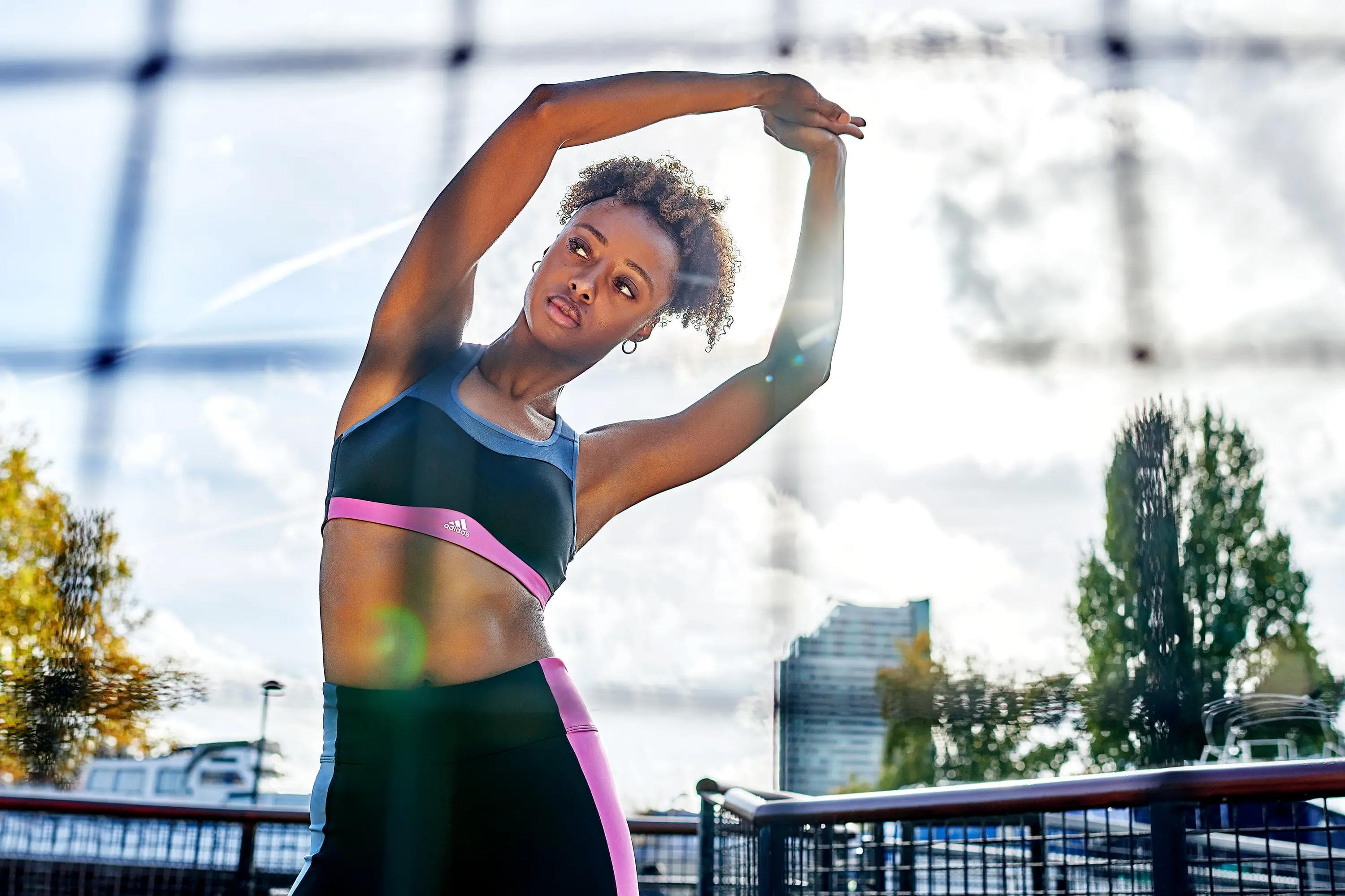 female athlete performing overhead stretch outdoors while wearing adidas sportswear, activewear campaign photography
