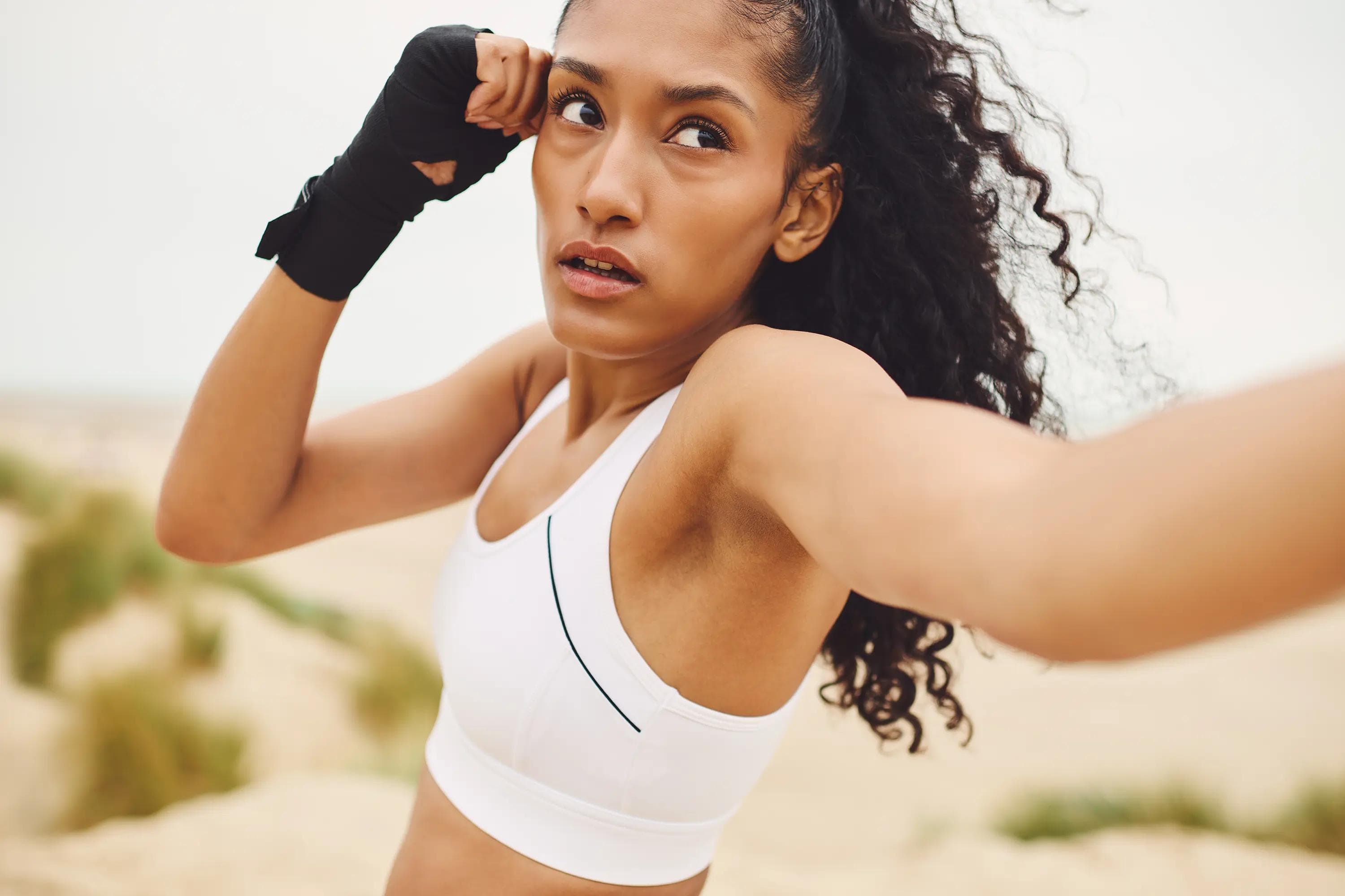 close up action portrait of female fighter executing a front kick toward the camera during beach training