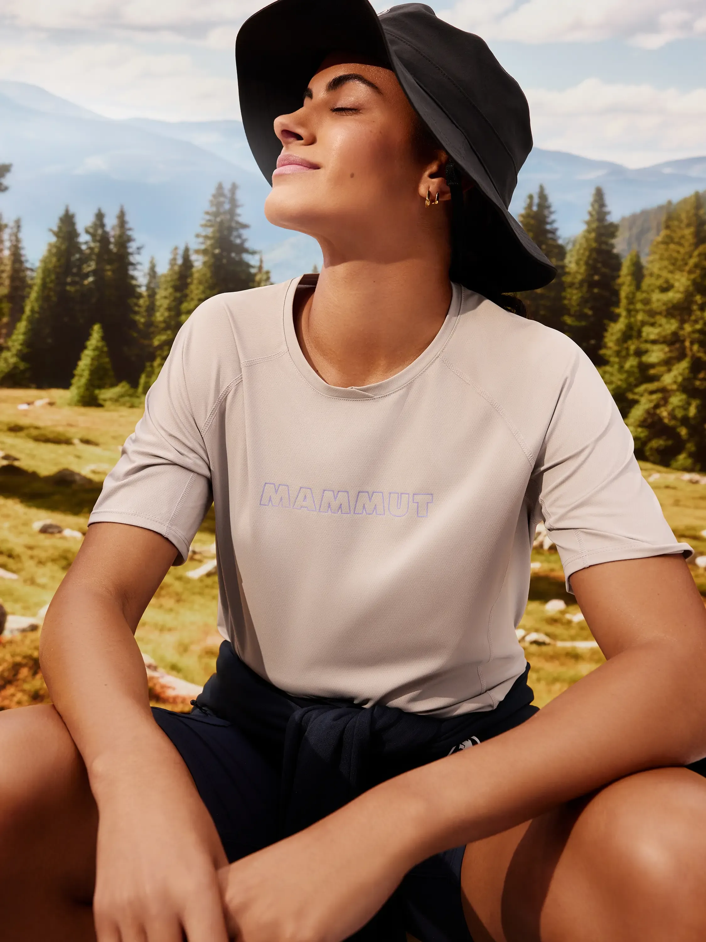 modello con giacca outdoor blu e bastoncini da trekking, montagne sullo sfondo