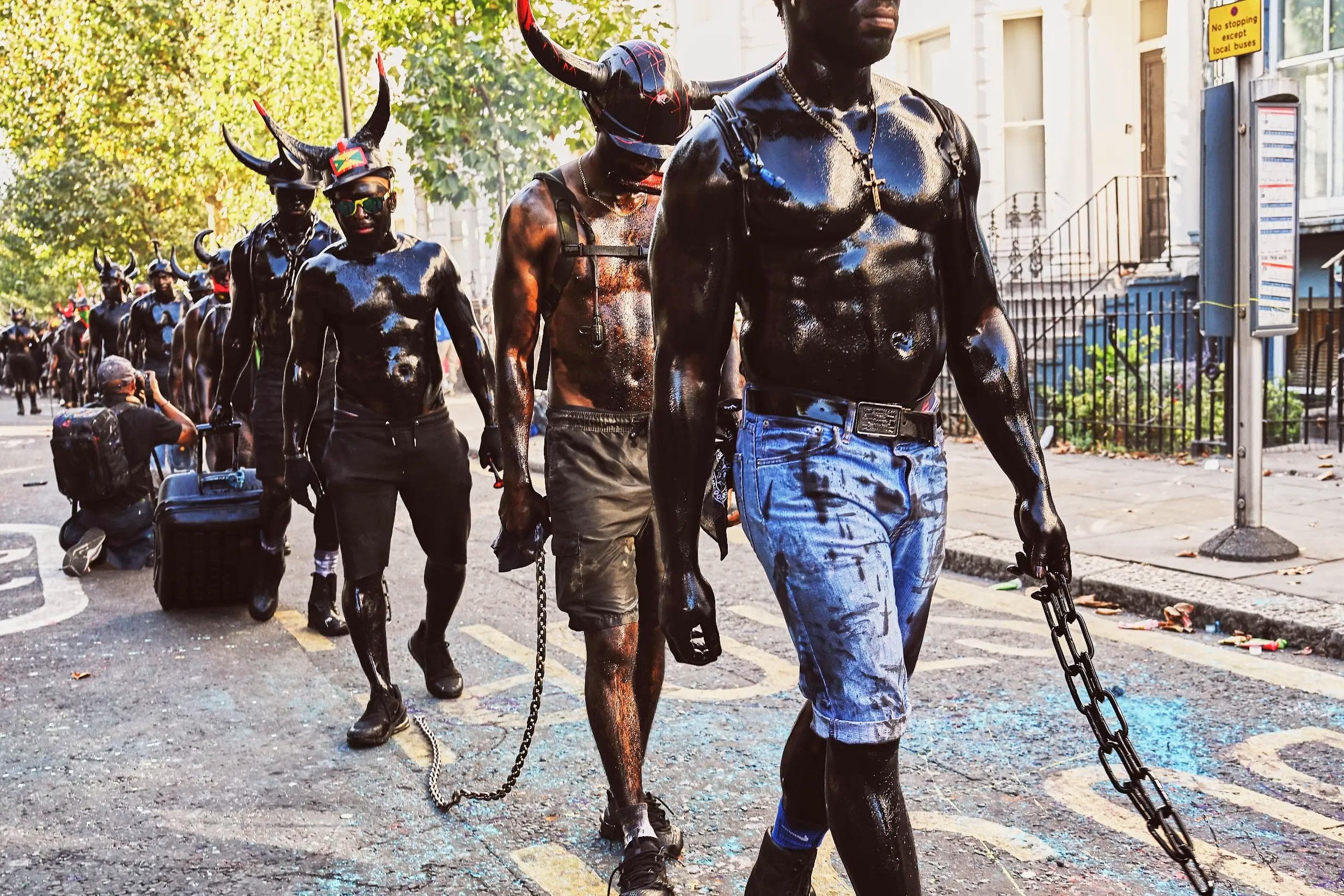 close portrait of Jab Jab performer covered in black paint with chains and horned helmet during carnival ritual