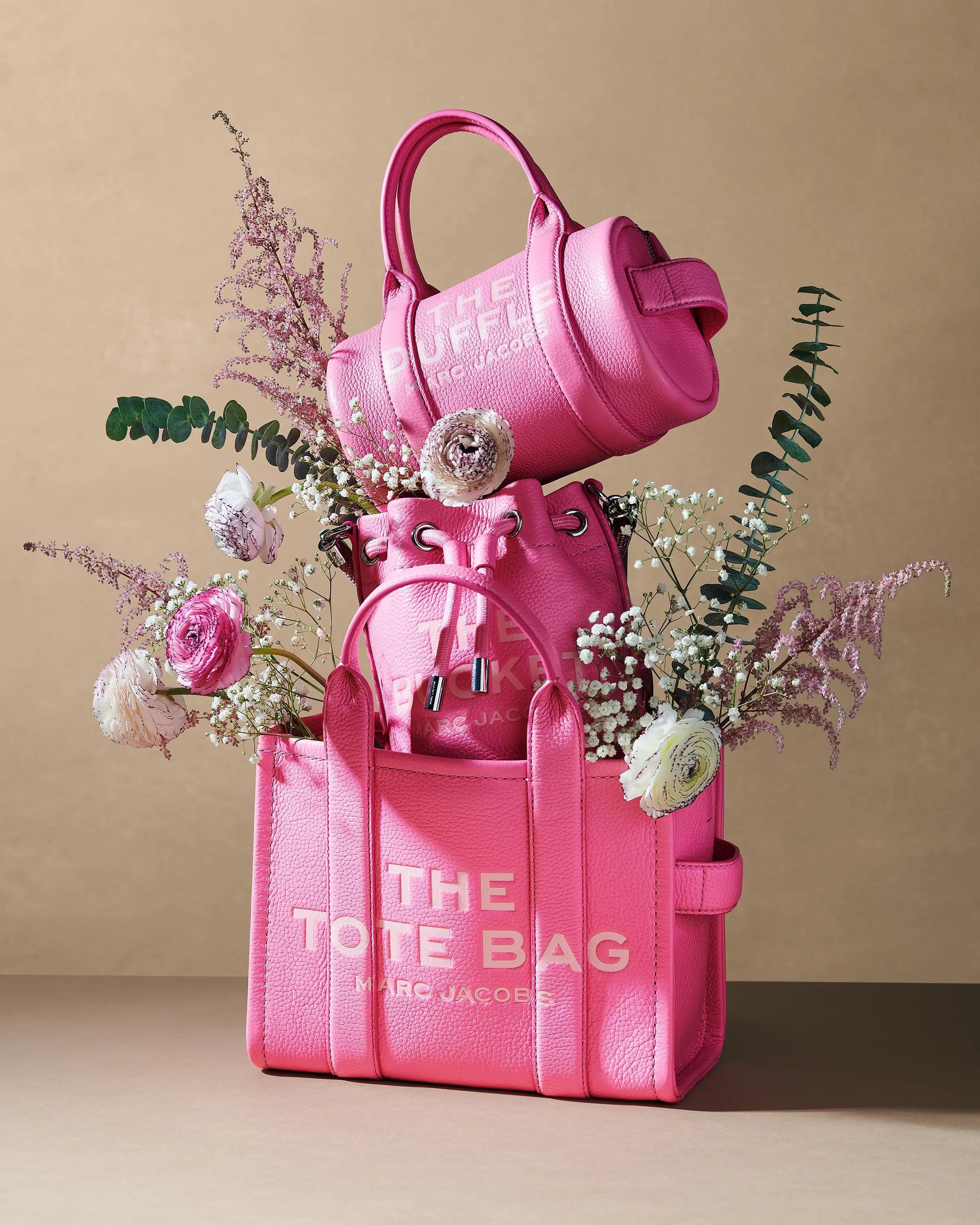 pink Marc Jacobs The Bucket bag filled with multicoloured gerbera daisies against warm beige backdrop, luxury accessories still life photography London
