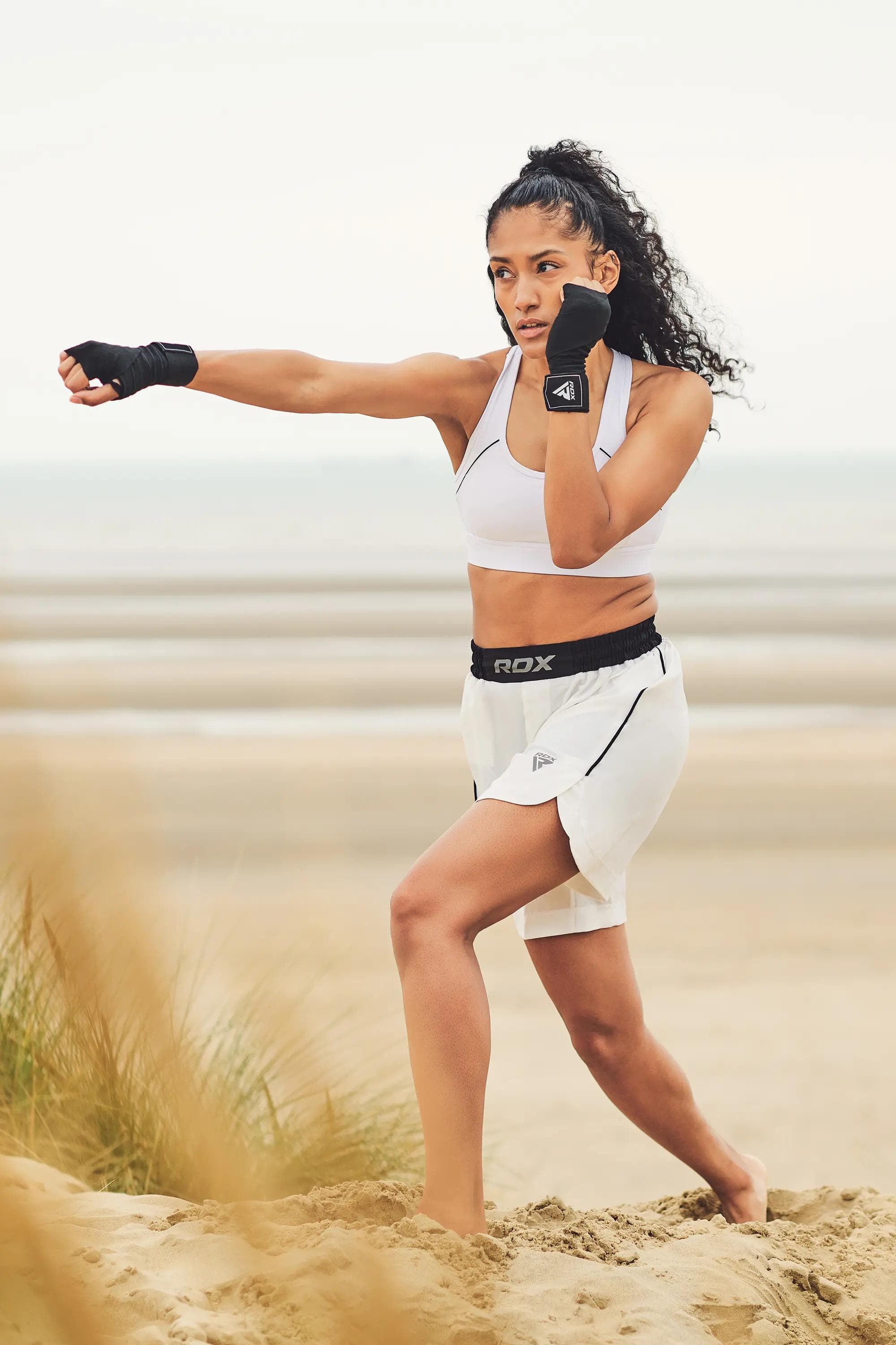 female combat athlete throwing a straight punch during outdoor beach training in RDX apparel