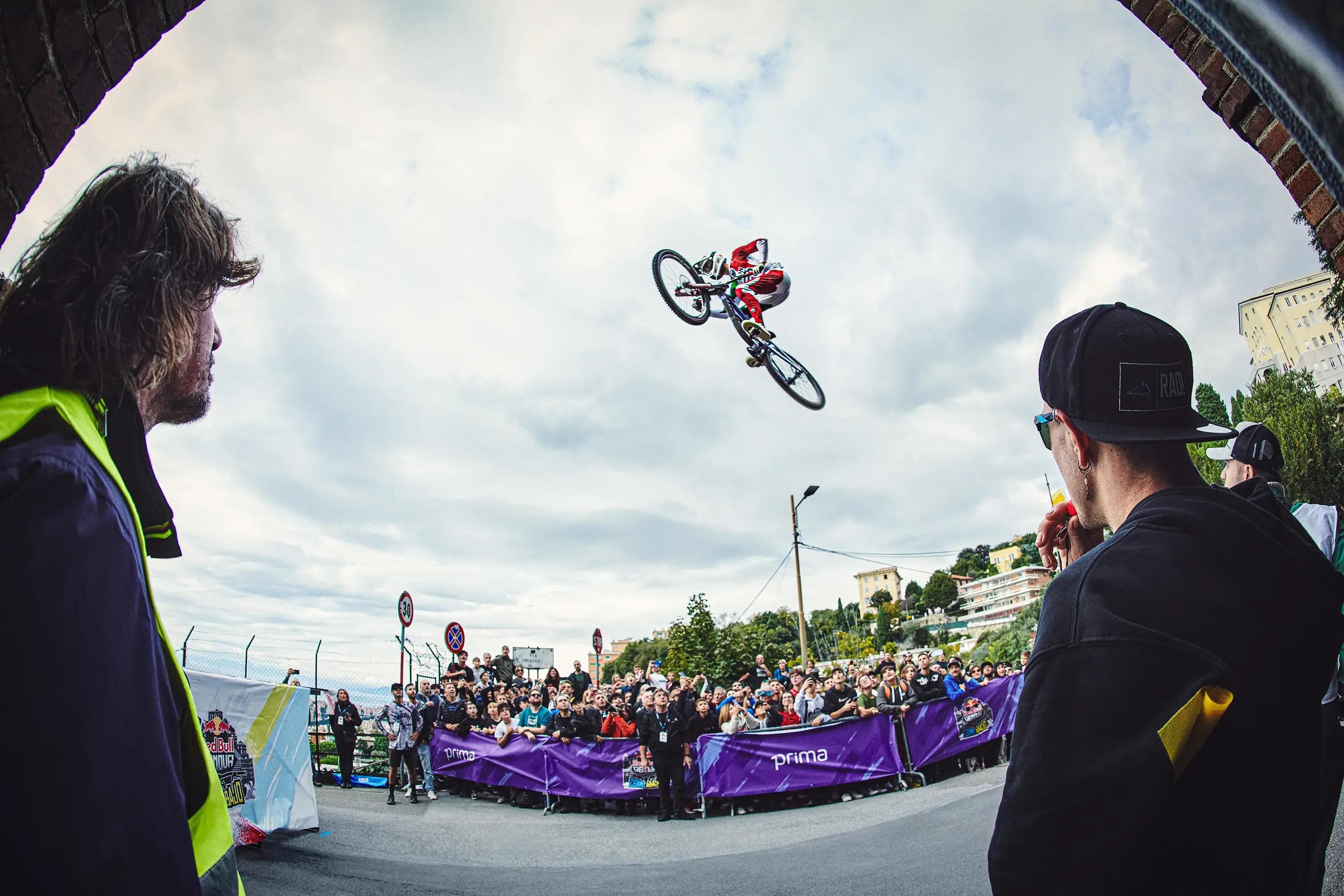 crowd watching downhill rider mid air framed by urban street, high energy moment, extreme cycling photography